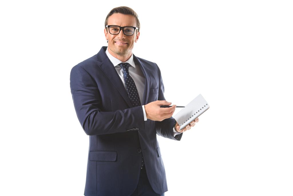 χαμογελώντας επιχειρηματία σε γυαλιά δείχνει από στυλό πάνω σε βιβλίο απομονωθεί σε λευκό φόντο  - Φωτογραφία, εικόνα