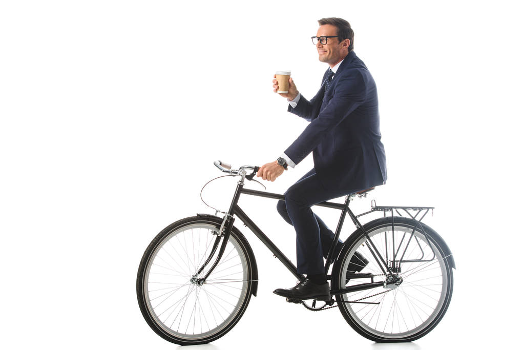lachende zakenman in brillen fiets en houden papieren kopje koffie geïsoleerd op witte achtergrond  - Foto, afbeelding