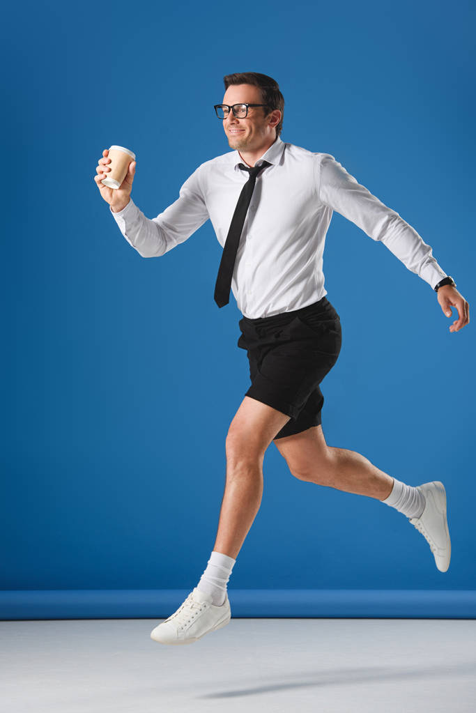 hombre feliz sosteniendo taza de café desechable mientras salta y mirando hacia otro lado en azul
 - Foto, imagen