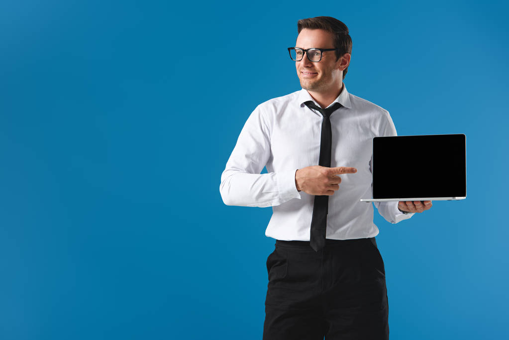 uśmiechnięty mężczyzna w okularach, wskazując palcem na laptopie z pustego ekranu i patrząc od hotelu na niebieskim tle - Zdjęcie, obraz