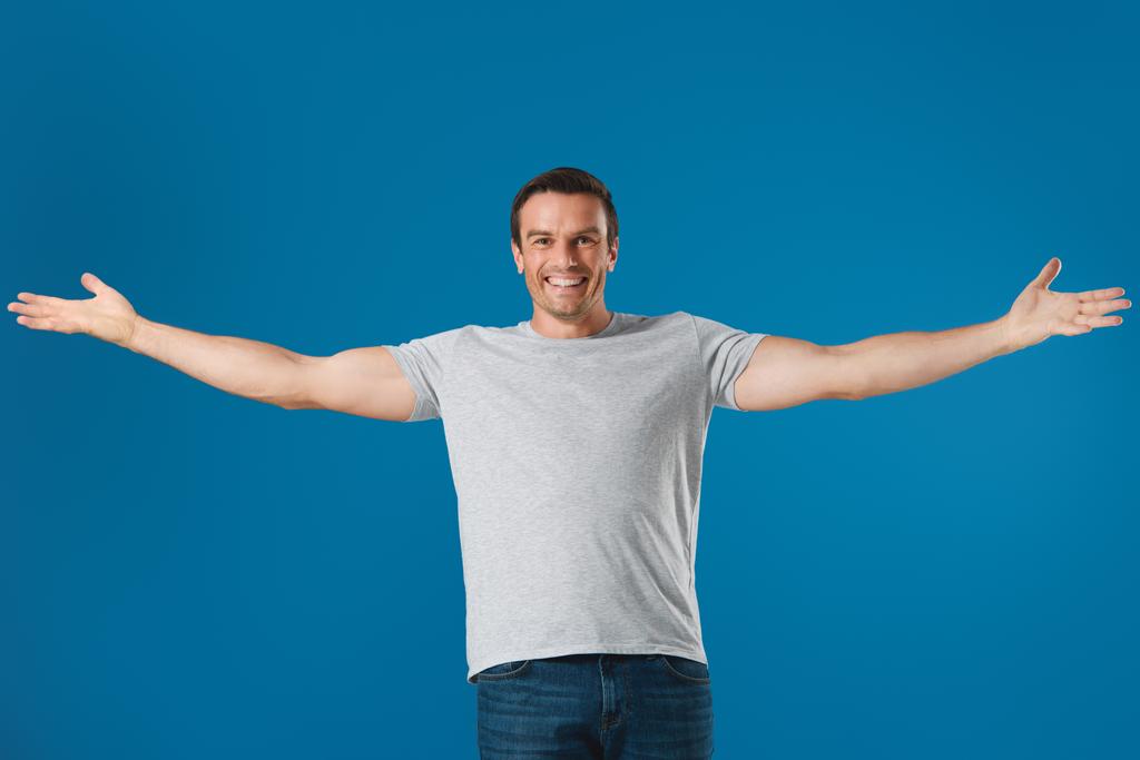 homem alegre de pé com os braços abertos e sorrindo para a câmera isolada em azul
 - Foto, Imagem