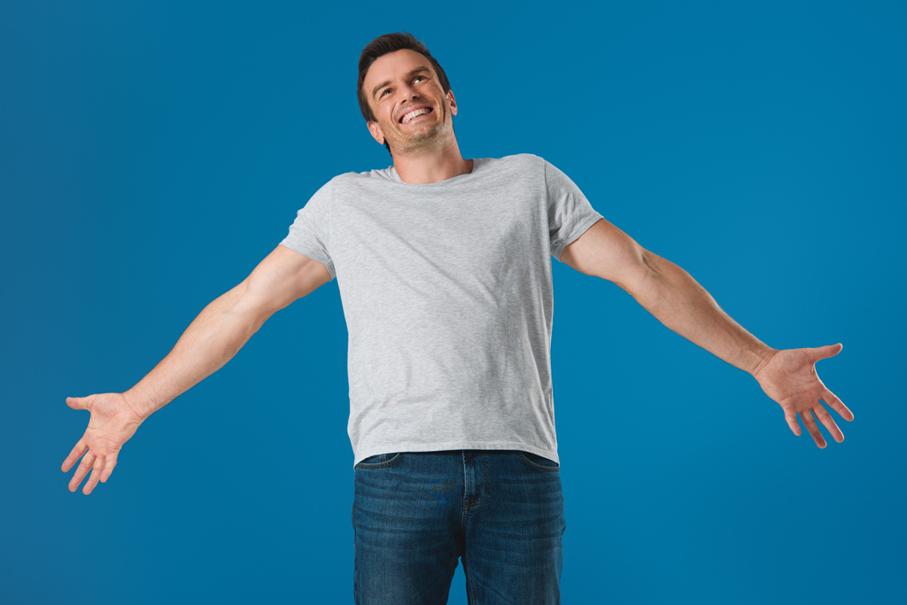 happy man standing with open arms and looking up isolated on blue - Photo, Image
