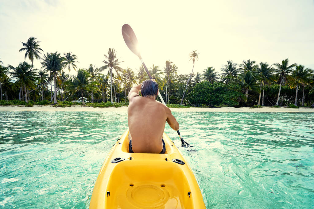 Молодий чоловік веслує на морському каяку в тропічній спокійній лагуні
. - Фото, зображення