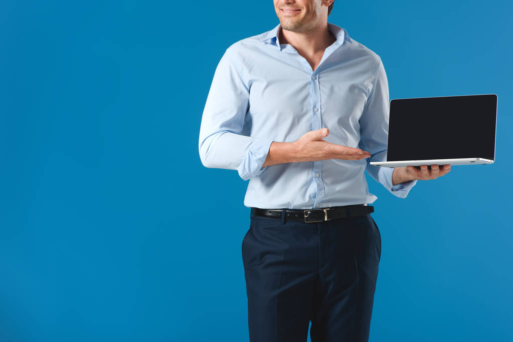 abgeschnittene Aufnahme eines lächelnden Mannes mit Laptop und leerem Bildschirm isoliert auf blau - Foto, Bild