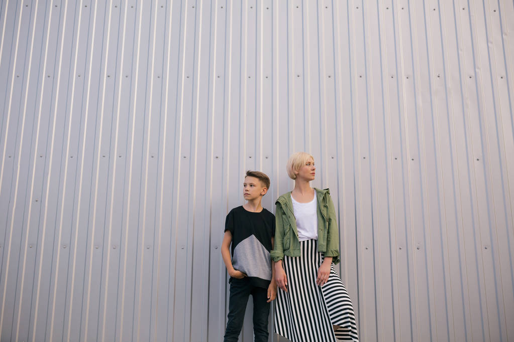 vista de ángulo bajo de hermosa madre e hijo con estilo mirando hacia otro lado mientras están de pie juntos en la calle
 - Foto, imagen
