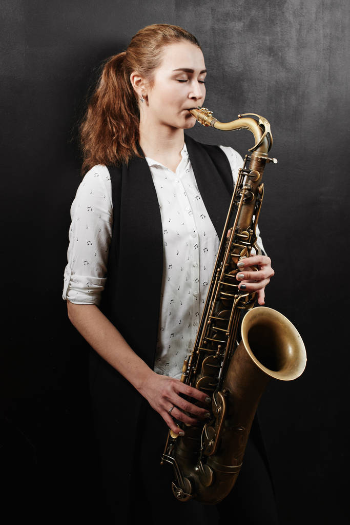 Young woman playing saxophone on black background - Photo, Image