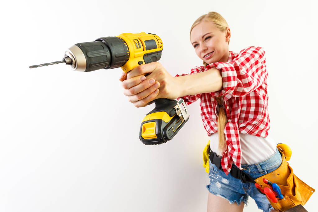 Nuori päättäväinen nainen, joka käyttää poraa kodin kunnostamiseen. Naispuolinen rakennustyöntekijä, jolla on poraustyökalun porausseinä. - Valokuva, kuva