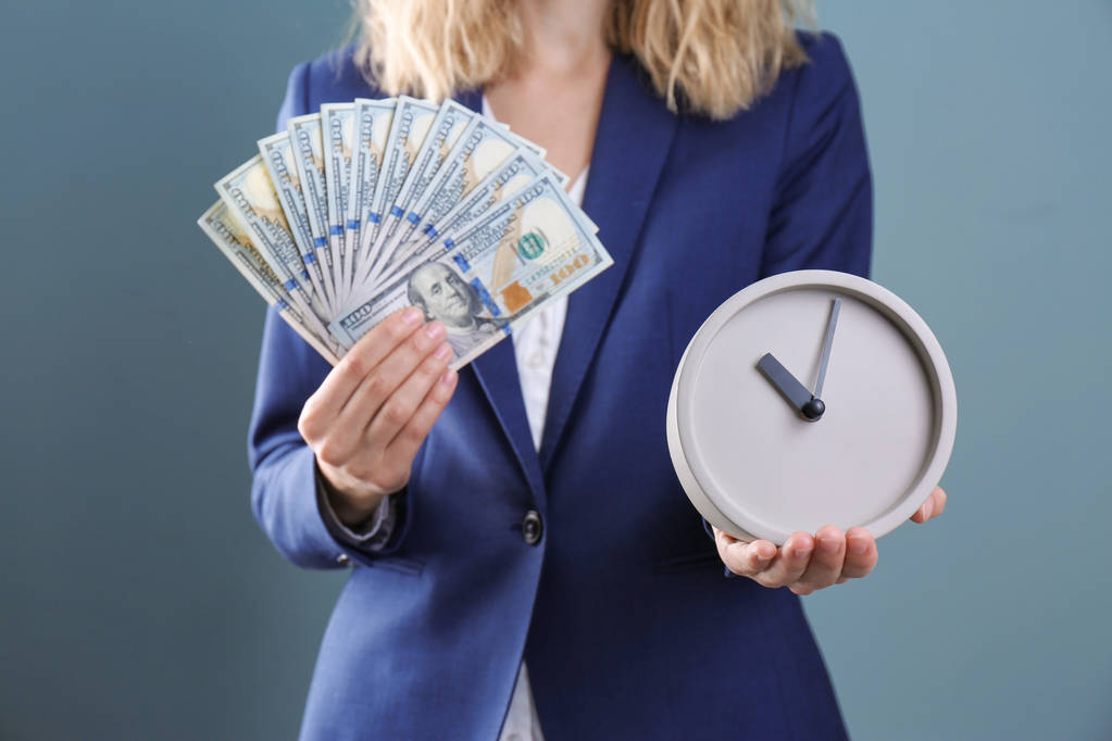 Young businesswoman holding clock and money on color background. Time management - Photo, Image