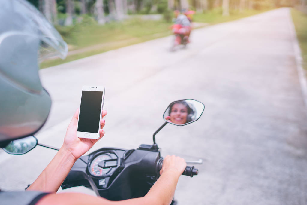 Mujer joven en casco sosteniendo teléfono inteligente mientras conduce motocicleta
.  - Foto, imagen
