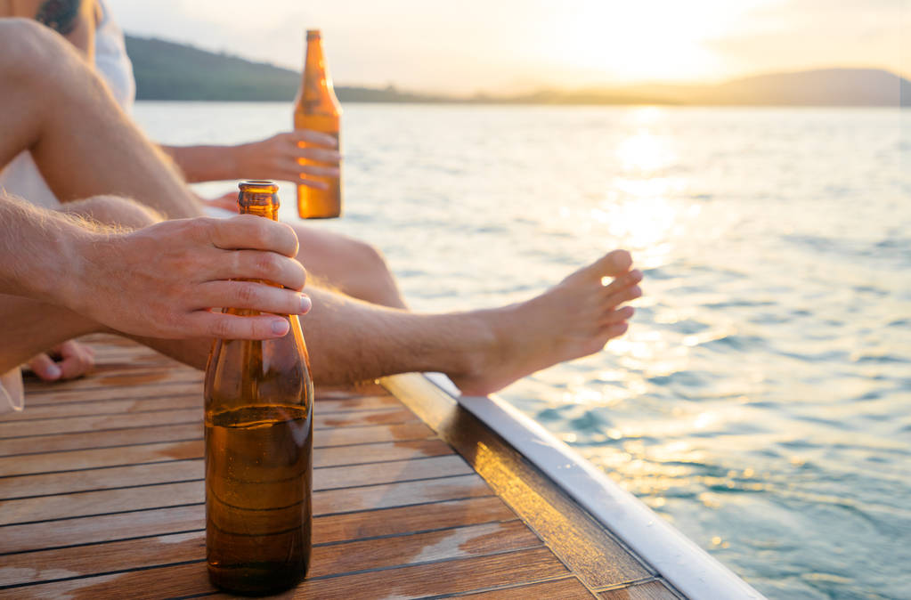 Εσωτερικη αρσενική χέρι που κρατά το μπουκάλι μπύρας για το γιοτ να πλέουν στη θάλασσα. - Φωτογραφία, εικόνα