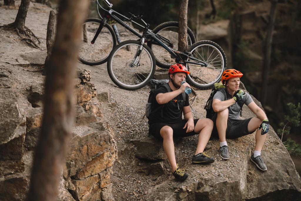 若いトライアル自転車乗車後岩の崖にリラックスして食事のハイアングル - 写真・画像