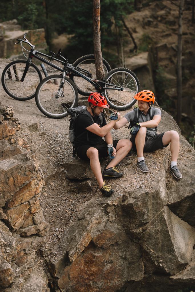 vista de ángulo alto de los jóvenes ciclistas de trial que se relajan en el acantilado rocoso después de montar y darse la mano
  - Foto, imagen