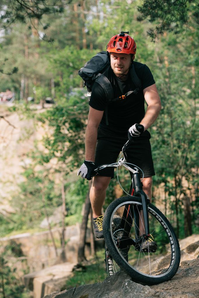 sonriente ciclista de trial masculino en casco protector montando en bicicleta de montaña en el bosque
 - Foto, Imagen