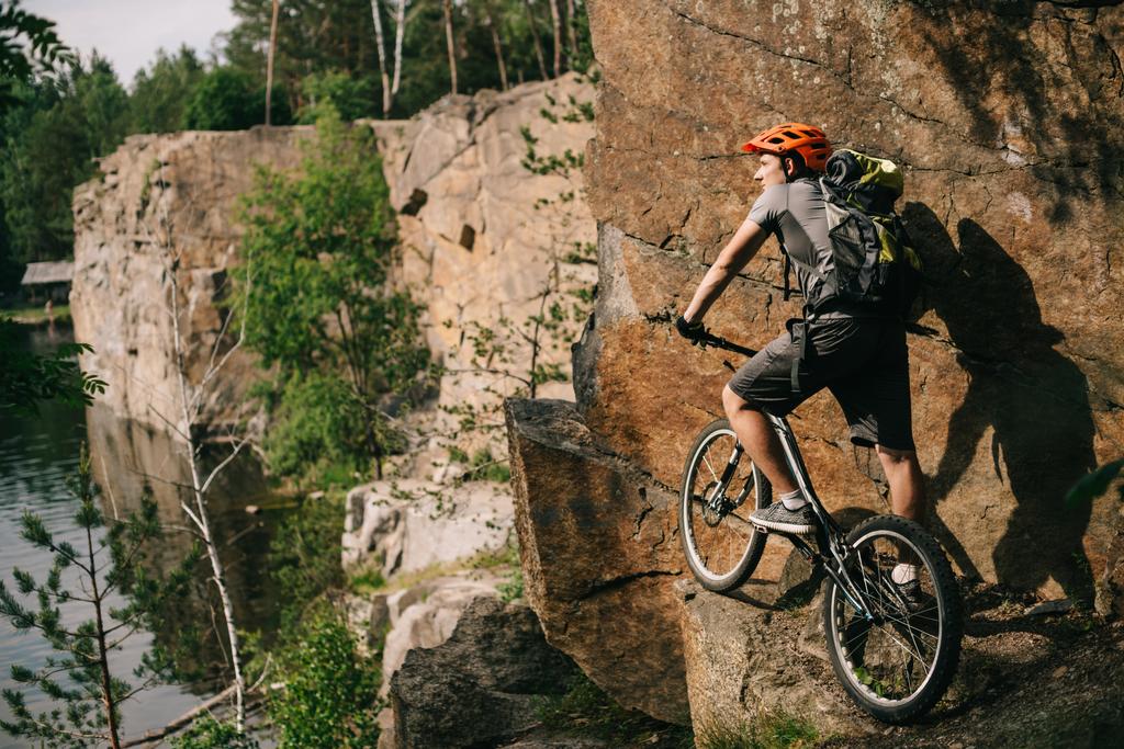 Junger Trial-Biker mit Fahrrad steht auf Klippe und blickt auf schöne Landschaft - Foto, Bild