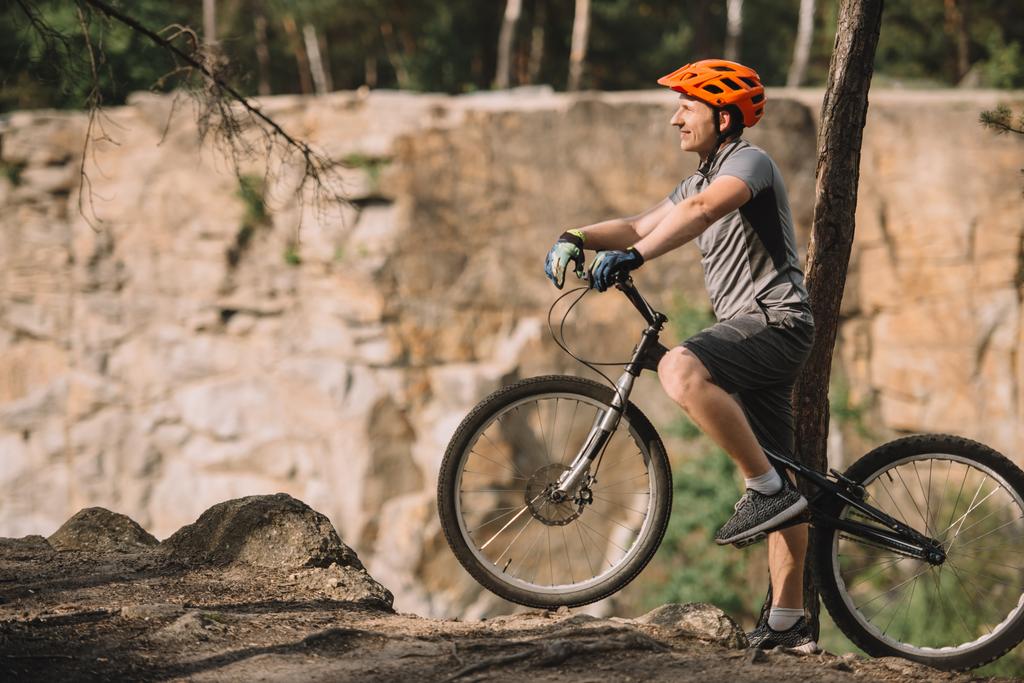 Seitenansicht eines hübschen jungen Mannes, der mit einem Trial-Bike im Wald steht - Foto, Bild