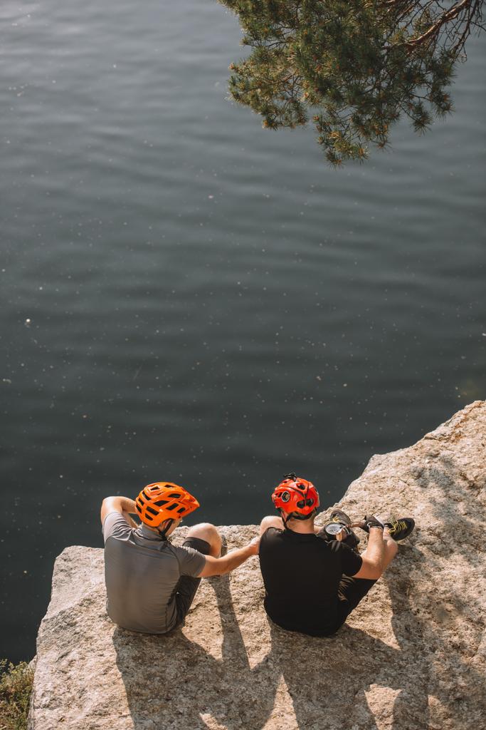 високий кут зору чоловіків-мандрівників у захисних шоломах, що їдять консервовану їжу на скелястій скелі над річкою
 - Фото, зображення