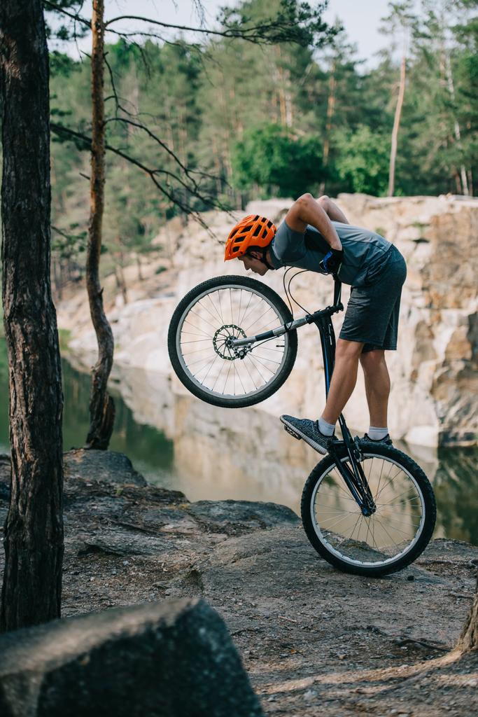 Junger Trial-Biker balanciert auf Hinterrad vor Waldsee - Foto, Bild