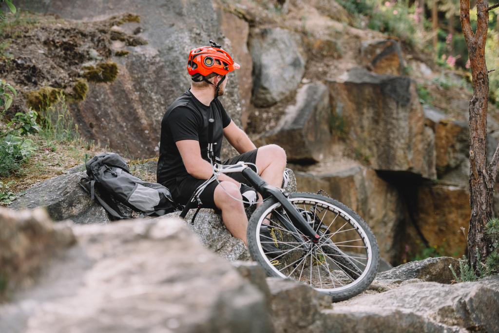 mladí zkušební biker odpočinkem na skalách s kolo venku a při pohledu na daleko - Fotografie, Obrázek
