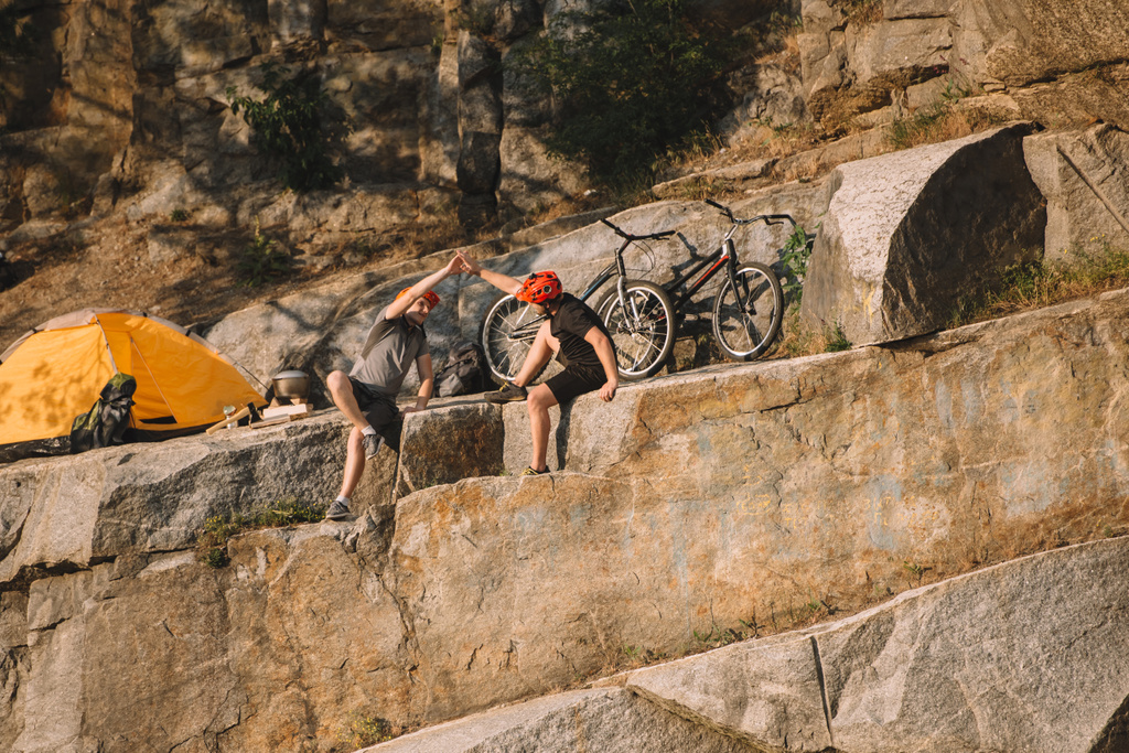 les motards d'essai se reposant et donnant cinq hauts les uns aux autres près de la tente et des cycles de montagne sur la falaise rocheuse
  - Photo, image