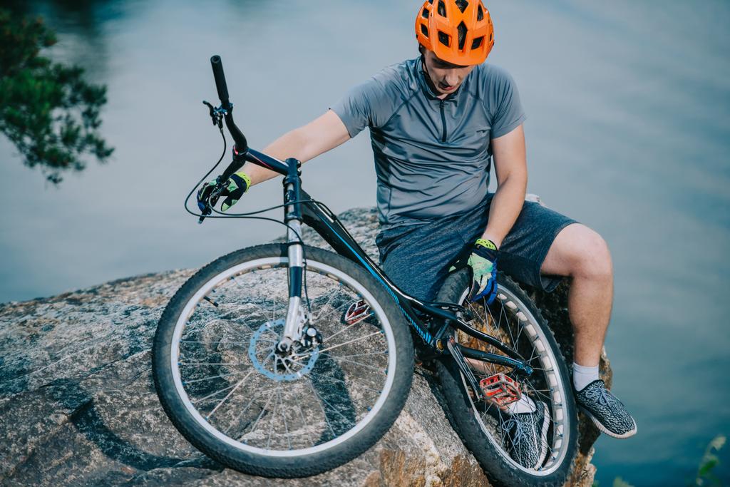 nuori kokeiluversio biker rentouttava kivinen kalliolla veden yli polkupyörällä
 - Valokuva, kuva