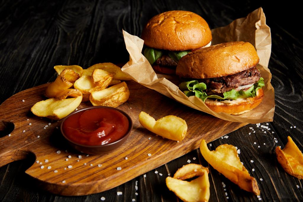 Tempting fast food diner with burgers and potatoes with sauce on cutting board - Photo, Image