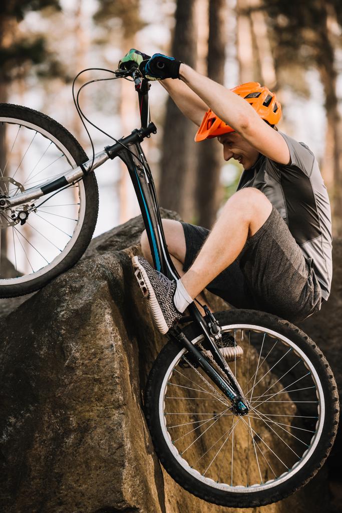 young trial biker climbing on rock with bicycle outdoors - Photo, Image