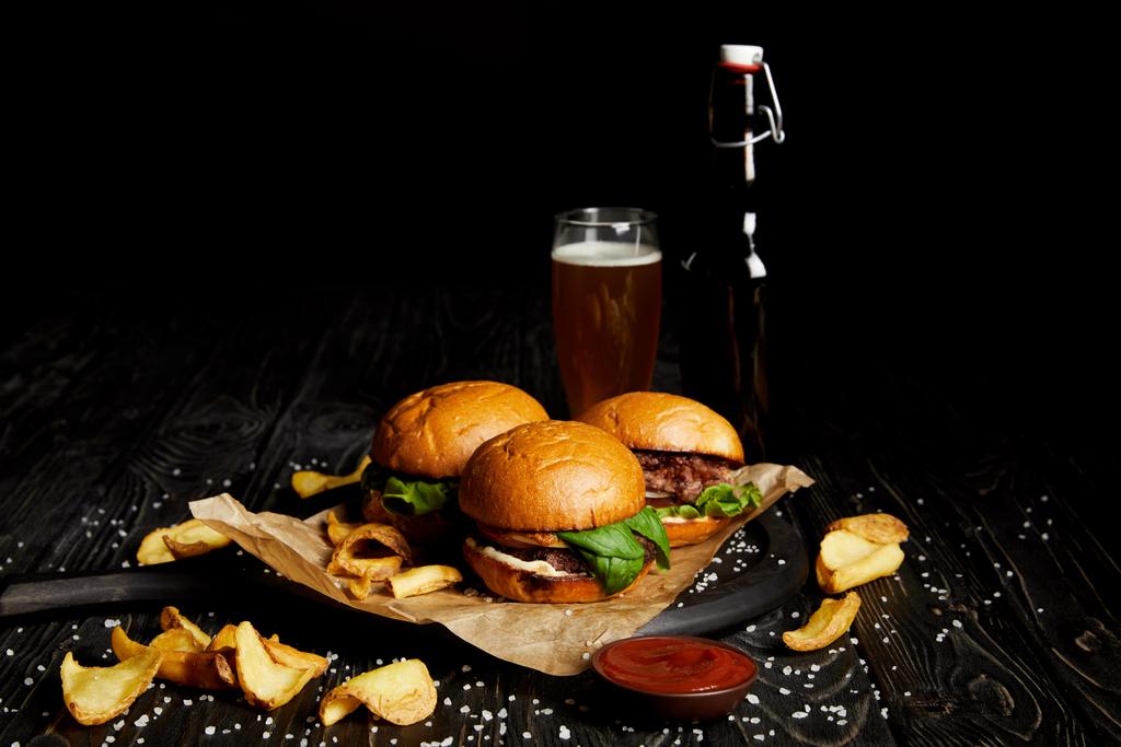 Joukko roskaruokaa hampurilaisilla ja ranskalaisilla perunoilla pöydällä oluella pullossa ja lasissa
 - Valokuva, kuva