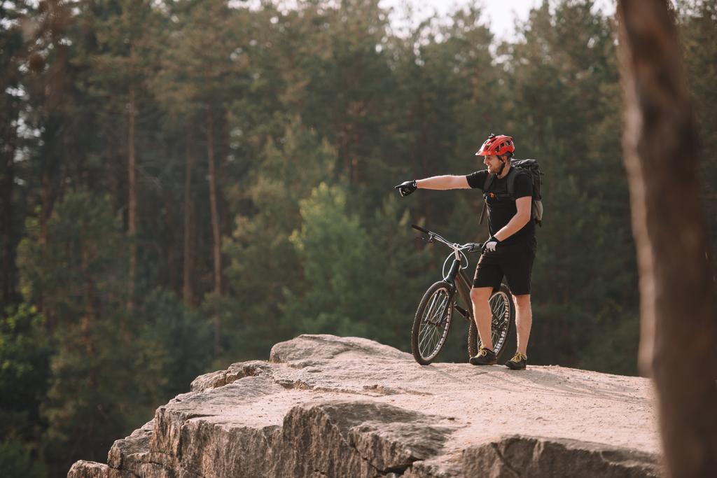 молодий пробний байкер, що стоїть на скелястій скелі на відкритому повітрі і вказує десь
 - Фото, зображення