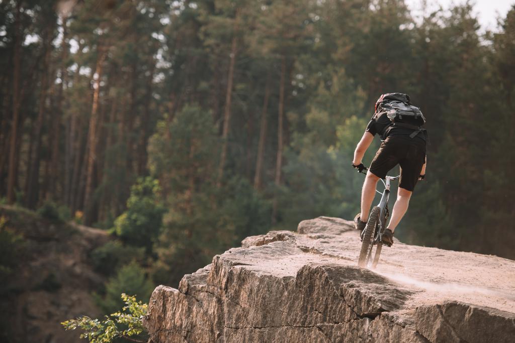 vista trasera del joven ciclista de trial cabalgando sobre rocas al aire libre
 - Foto, imagen