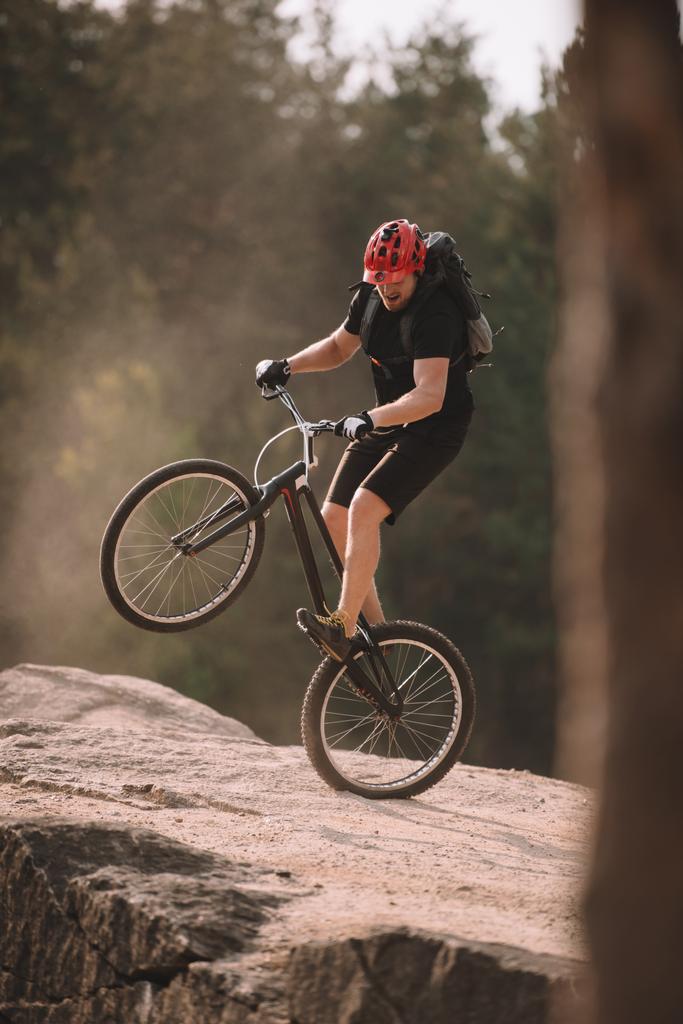 красивый судебный байкер балансирует на заднем колесе на скалах на открытом воздухе
 - Фото, изображение