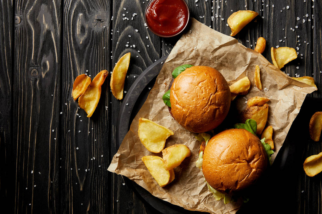 Vista superior de tentadoras hamburguesas de comida rápida y papas doradas sobre papel artesanal
 - Foto, imagen