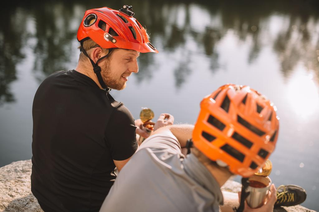 aktiiviset nuoret matkailijat syövät säilykkeitä retkeilyssä veden pinnan edessä
 - Valokuva, kuva
