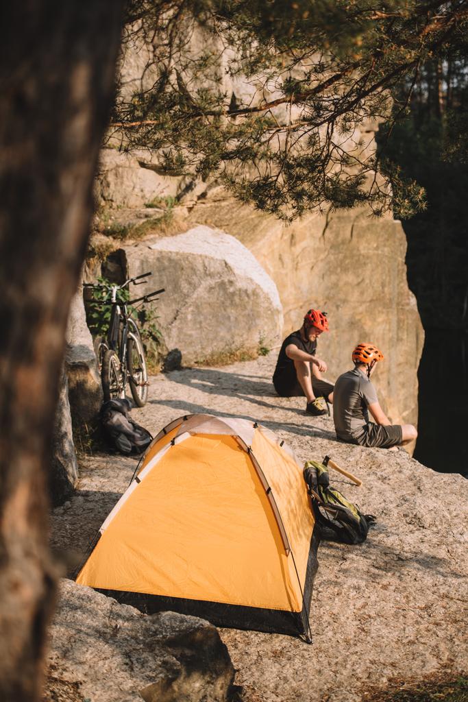 hoge hoekmening van trial bikers ontspannen op rotsachtige klip met camping tent - Foto, afbeelding