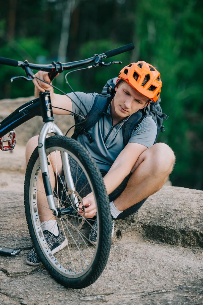 guapo joven ciclista de trial adjuntando rueda a la bicicleta al aire libre
 - Foto, Imagen