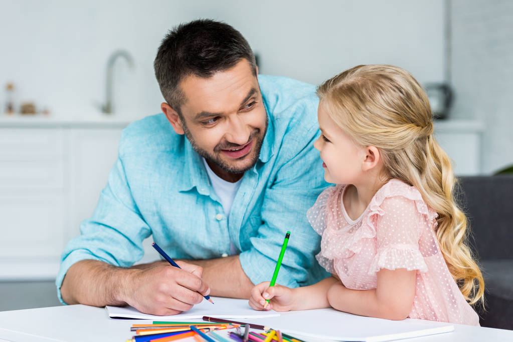 Gelukkig vader en dochter elkaar te glimlachen terwijl u tekent samen thuis - Foto, afbeelding