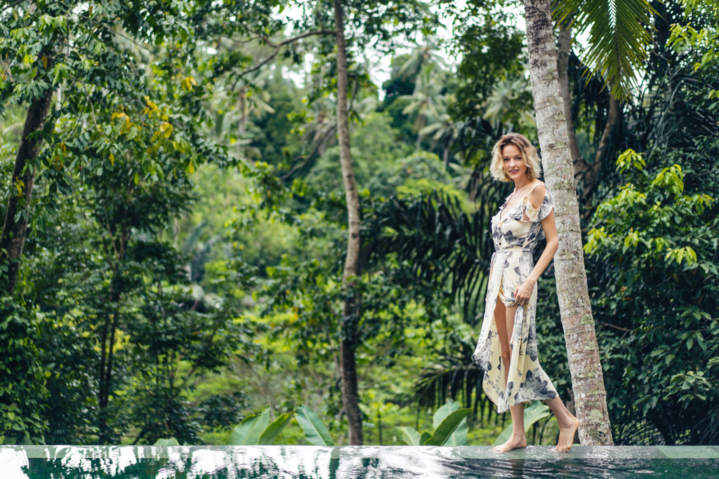 přitažlivá blondýnka v šatech, chůze v blízkosti bazénu se zelenými rostlinami na pozadí, ubud, bali, Indonésie - Fotografie, Obrázek