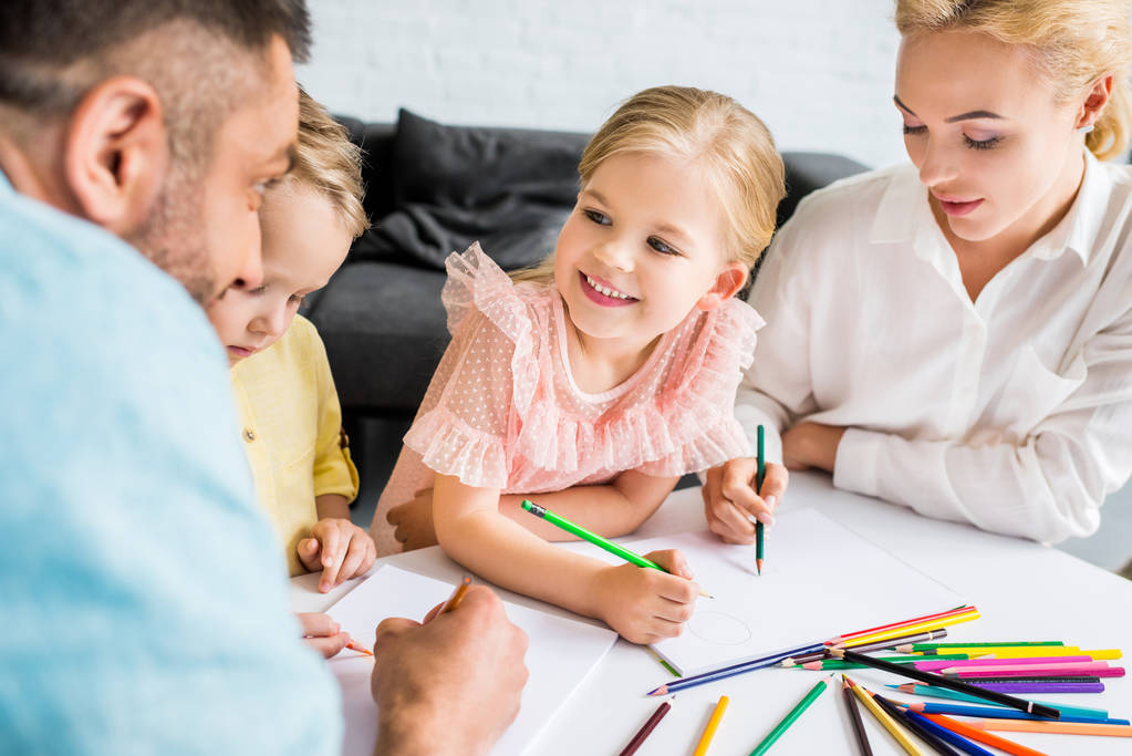 glückliche Familie mit zwei Kindern zeichnet zu Hause mit Buntstiften  - Foto, Bild