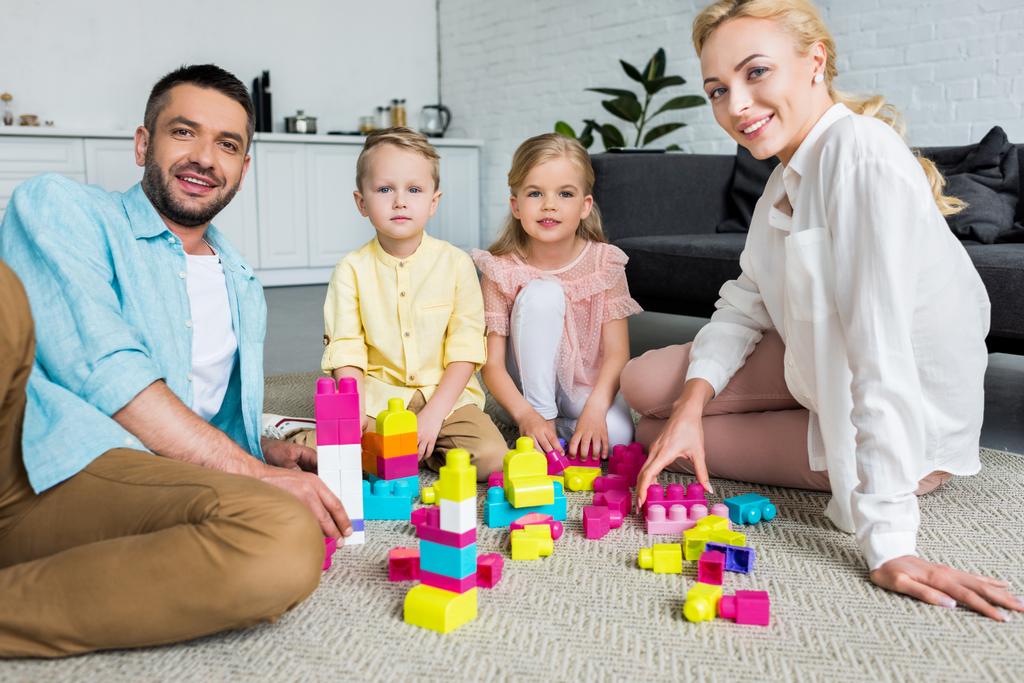 šťastná rodina se usmívá na kameru při hraní s barevnými bloky doma - Fotografie, Obrázek