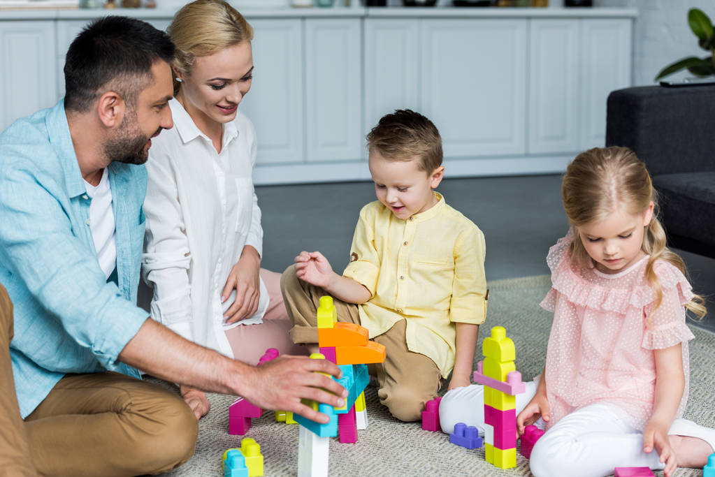 šťastní rodiče s roztomilé malé děti hrát si s barevnými bloky doma - Fotografie, Obrázek