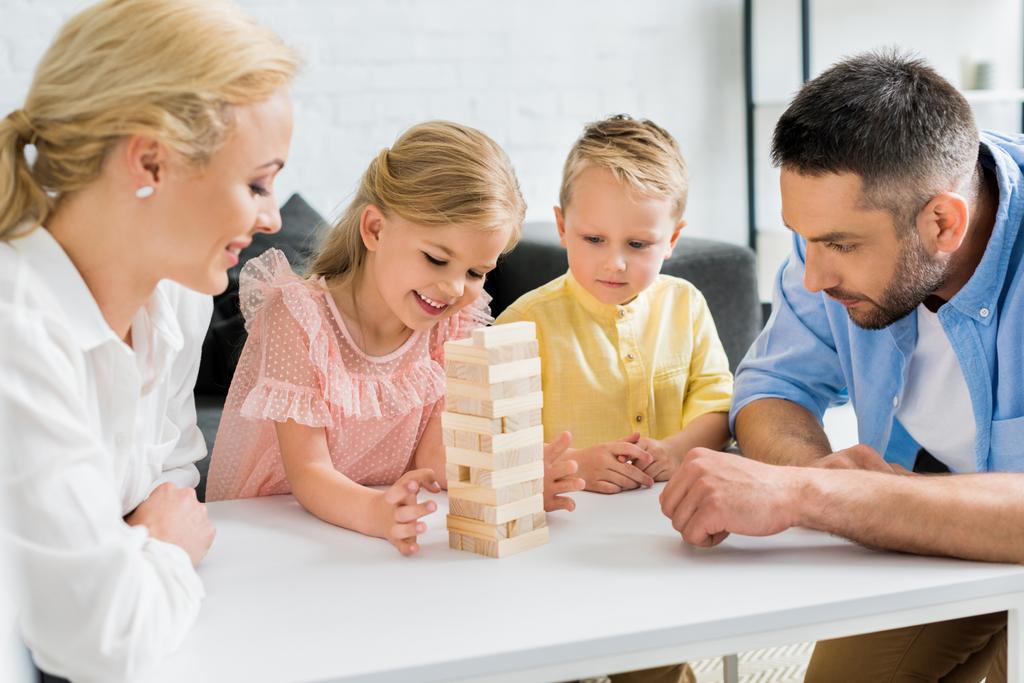 ευτυχισμένη οικογένεια με δύο παιδιά που έπαιζαν με ξύλινα μπλοκ στο σπίτι   - Φωτογραφία, εικόνα