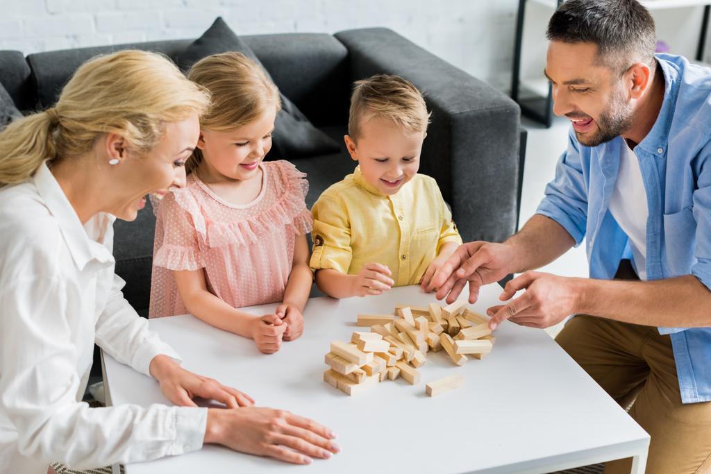 ευτυχισμένη οικογένεια με δύο παιδιά που παίζουν με ξύλινα μπλοκ στο σπίτι  - Φωτογραφία, εικόνα