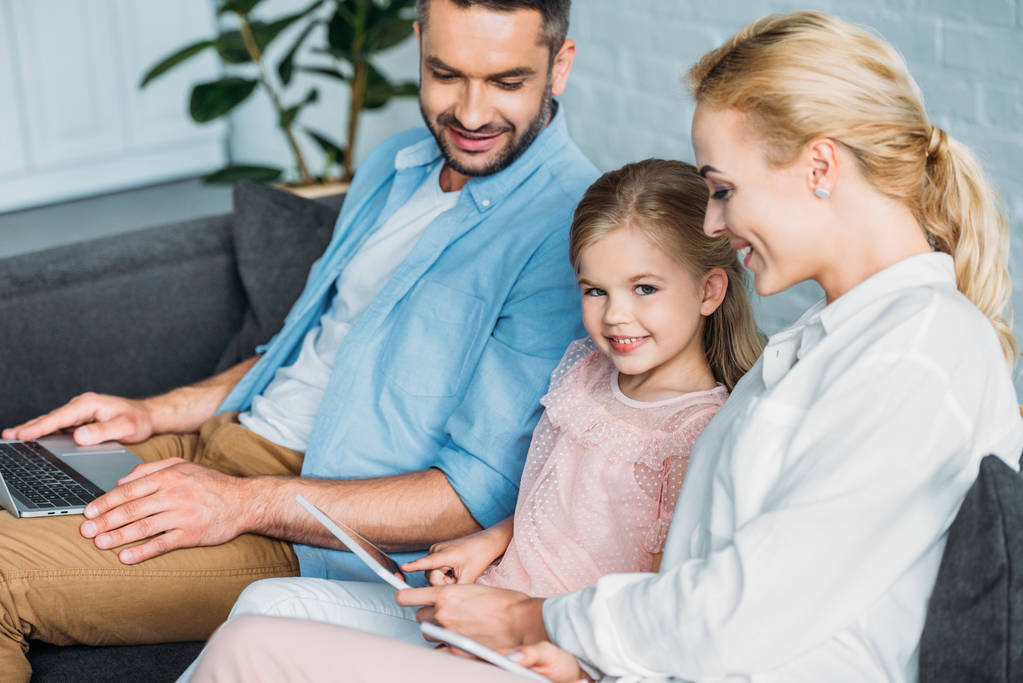 boldog család digitális eszközök használata közben ül a kanapén, otthon - Fotó, kép