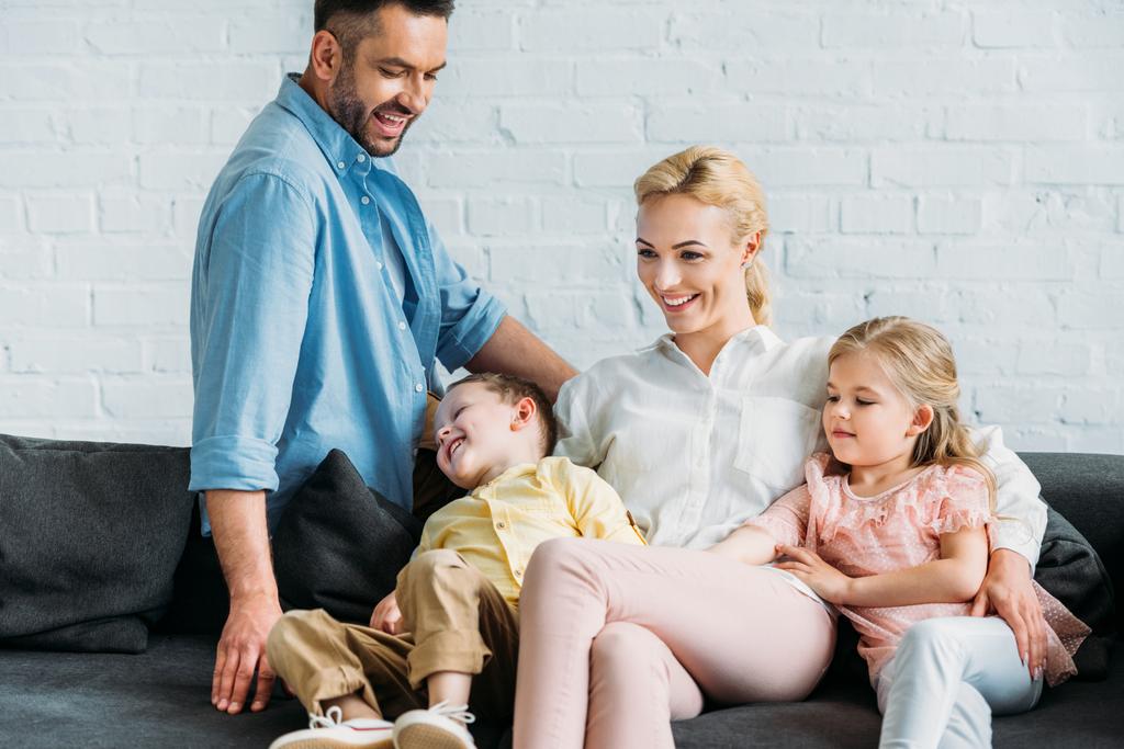 šťastná rodina s dvěma dětmi, zatímco sedí na gauči doma baví - Fotografie, Obrázek