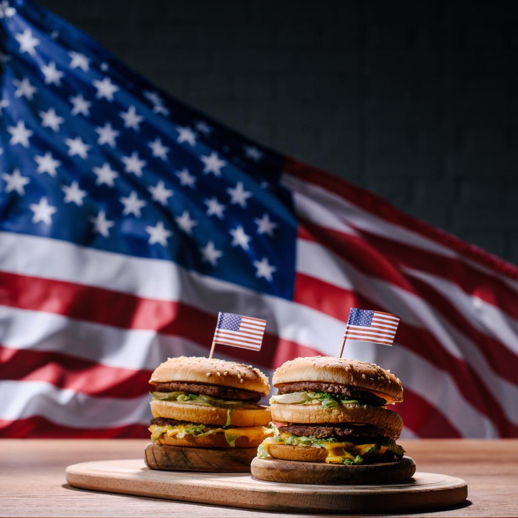 Amerika Birleşik Devletleri bayrağı sallayarak önünde ahşap kesme tahtası üzerinde lezzetli hamburger - Fotoğraf, Görsel