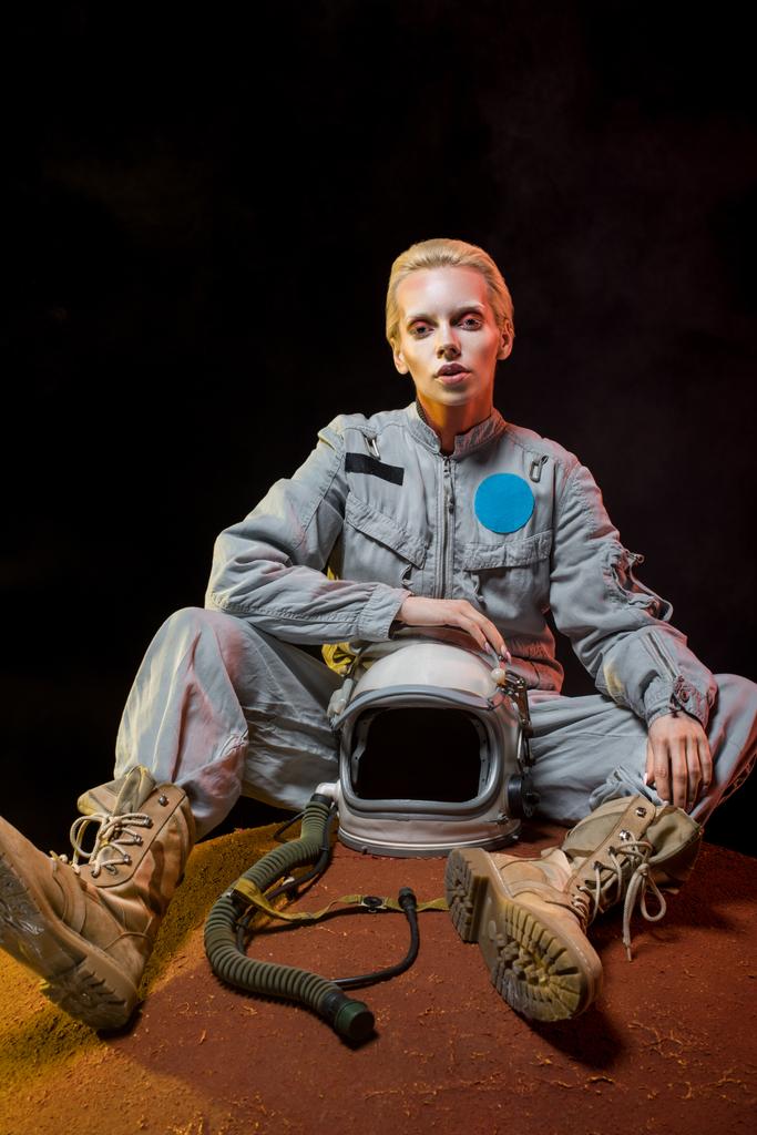 belle cosmonaute femelle en combinaison spatiale tenant casque et assise sur la planète
 - Photo, image