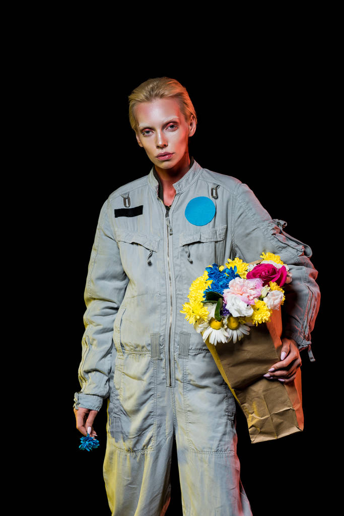 beautiful astronaut in spacesuit with flowers in paper bag, isolated on black - Photo, Image