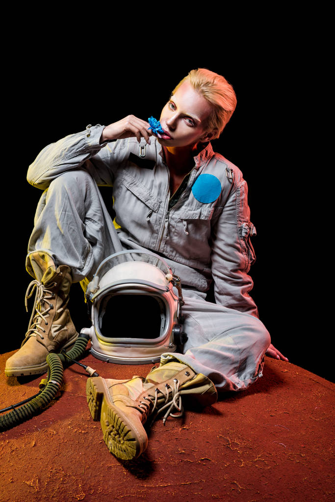 hermoso astronauta en traje espacial con flor y casco sentado en el planeta
 - Foto, imagen