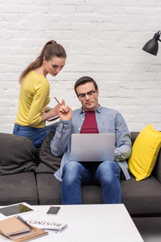 bel homme adulte travaillant avec un ordinateur portable tandis que sa femme lui parle par derrière à la maison
 - Photo, image