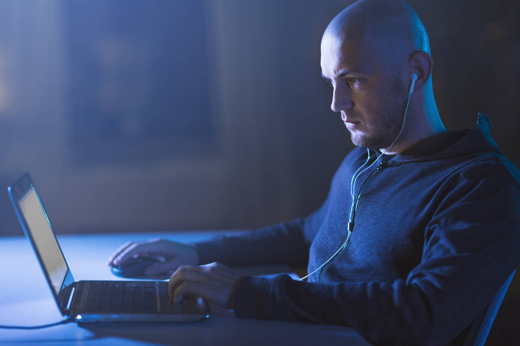 hacker en los auriculares escribiendo en el ordenador portátil en la habitación oscura
 - Foto, imagen