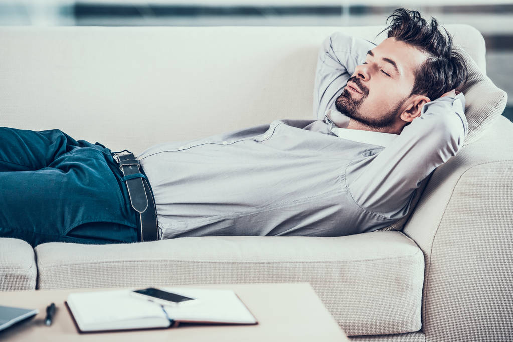 Κουρασμένος επιχειρηματίας γενειοφόρος κοιμάται στον καναπέ στο γραφείο - Φωτογραφία, εικόνα